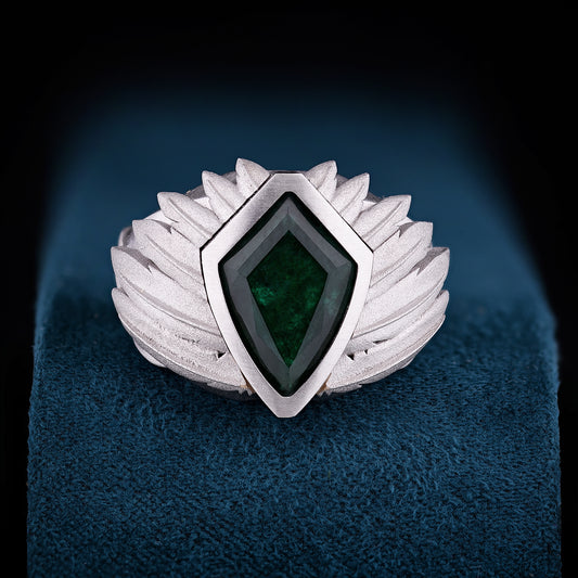 This ring wraps the hand in sculpted lightness, its emerald core held by a crown of carved wings.&nbsp;A symbol of ascent, identity, and the silent strength of becoming.